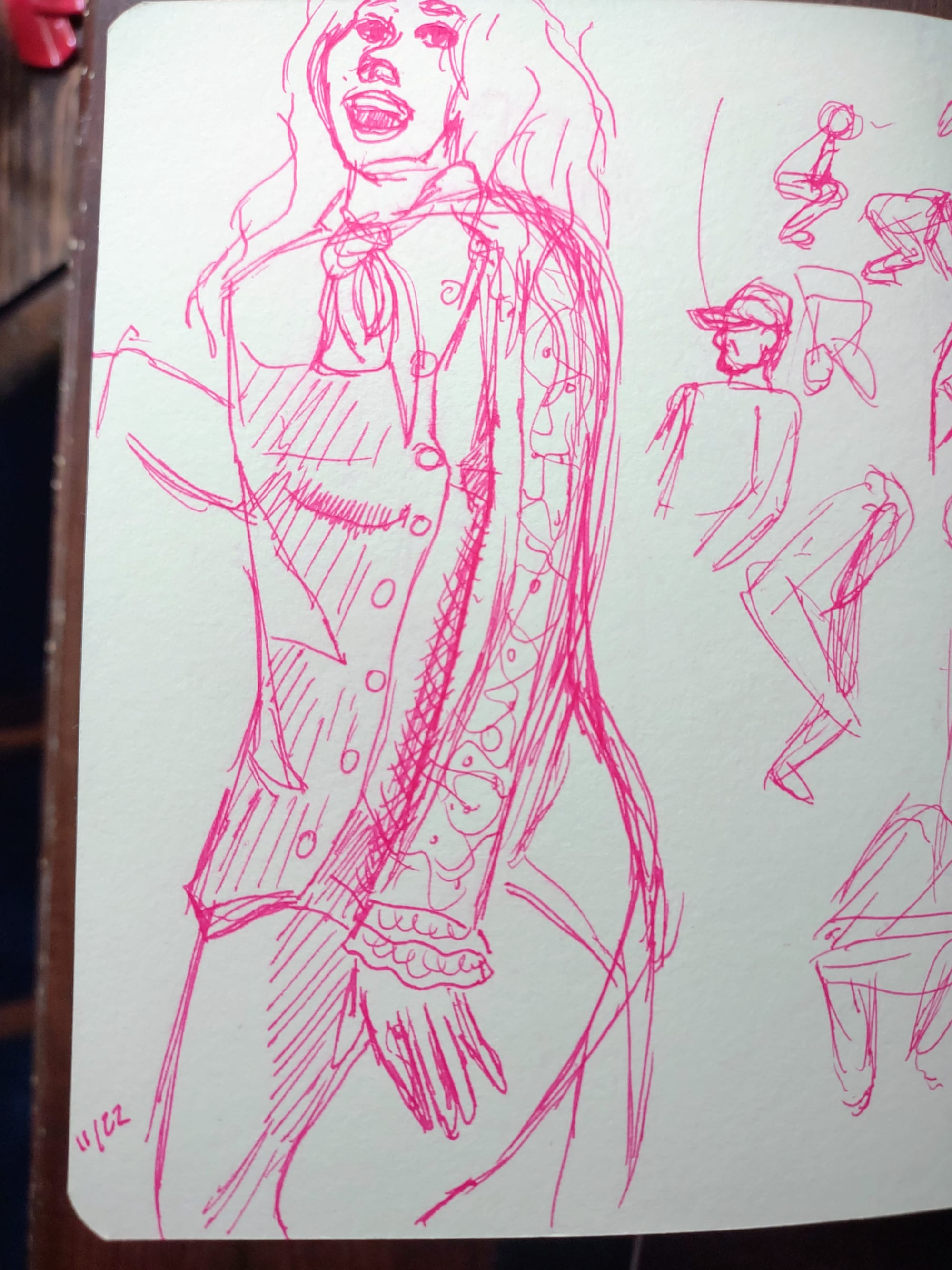 A sketchbook page with line drawings in pink ink, showing a wavy-haired woman smiling in a long buttoned jacket. Next to that are some small gesture drawings of crouching figures and a bust of someone in a baseball cap. 